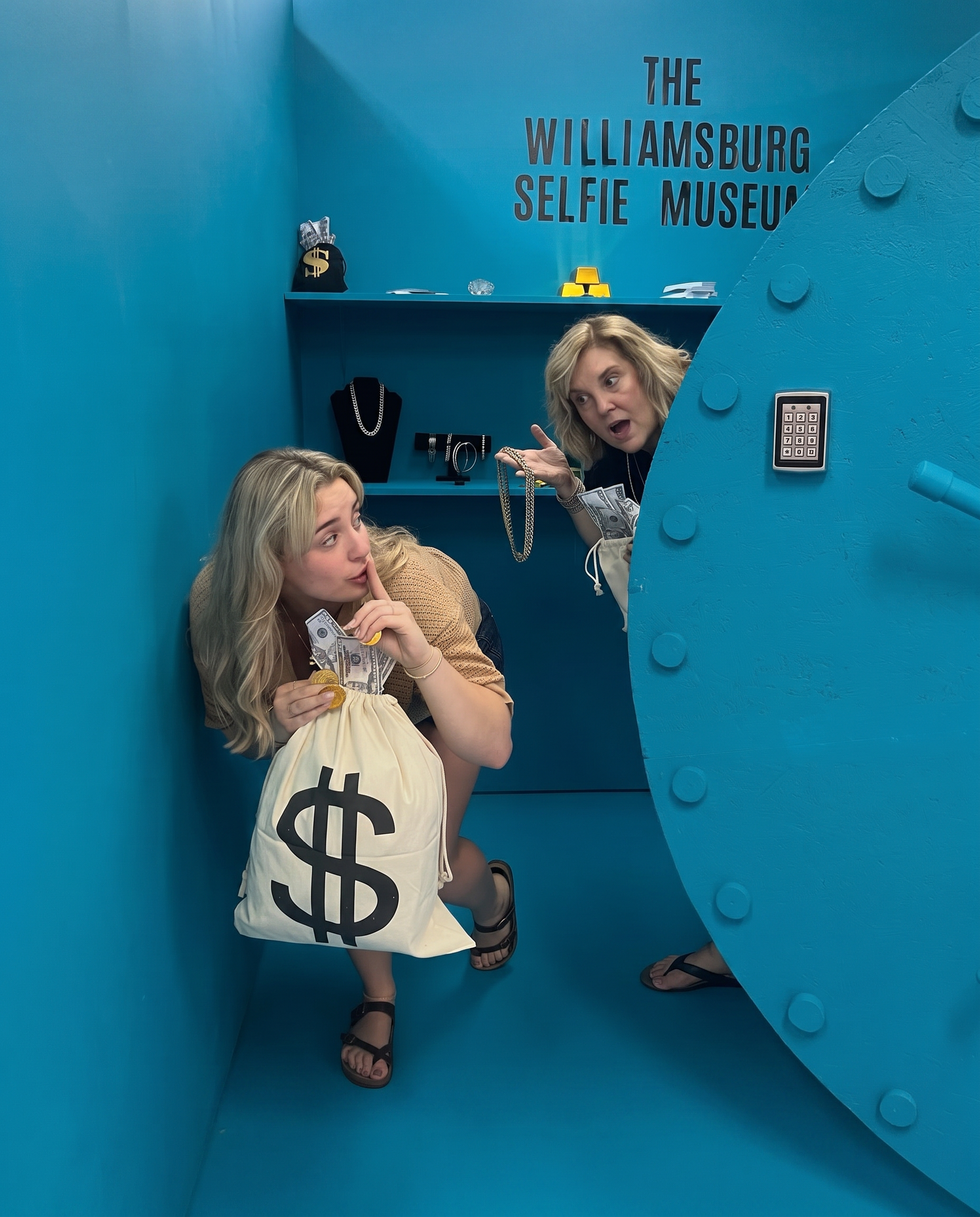 Guests posing with money bags inside the blue bank vault set at The Williamsburg Selfie Museum